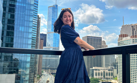 An image of Carla in a blue dress standing on a balcony in Chicago