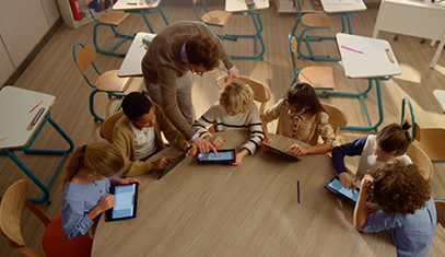 A teacher guides young students through an exercise as they sit on a large brown table
