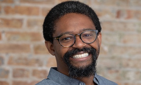 Ahmmad Brown, with a beard and glasses smiling
