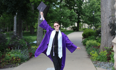 Sylvia proudly standing in their cap and gown under the arch.
